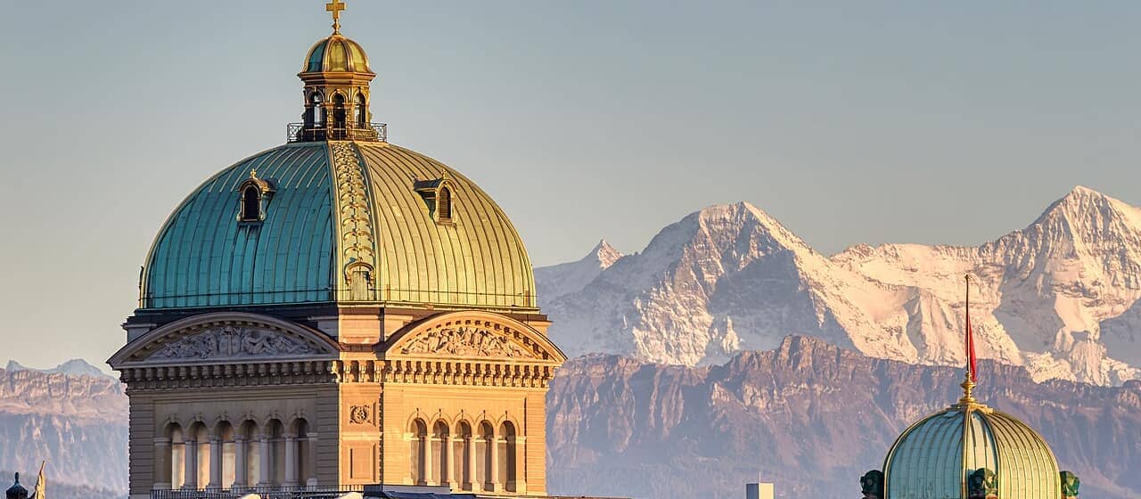 The domes of the Federal Palace (Bundeshaus) in Bern with the Alps behind.